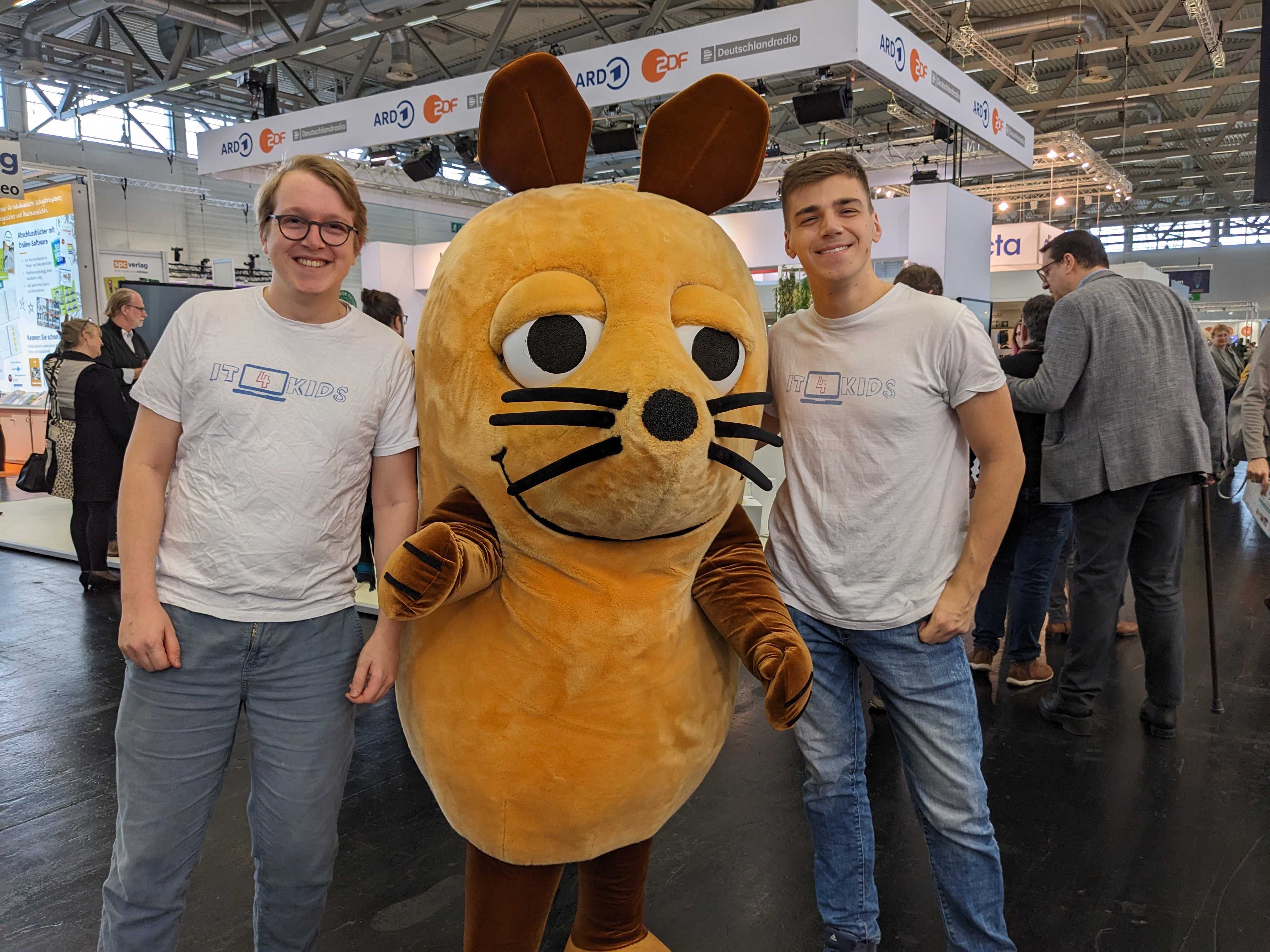 Zwei Teammitglieder stehen rechts und links von einem Maskottchen der WDR-Maus